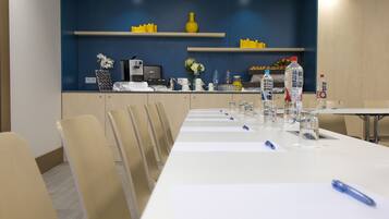 Un salón de conferencias con una larga mesa, sillas y varios servicios como botellas de agua, vasos y una máquina de café.