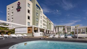 A hotel with a swimming pool, sun loungers, and umbrellas.