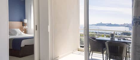 Habitación de hotel con cama, mesita de noche, lámpara y vista al mar a través de un ventanal corredizo.