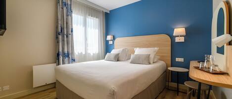 A hotel room with a large bed, bedside lamps, a small table with a tray, and a mirror on the wall.