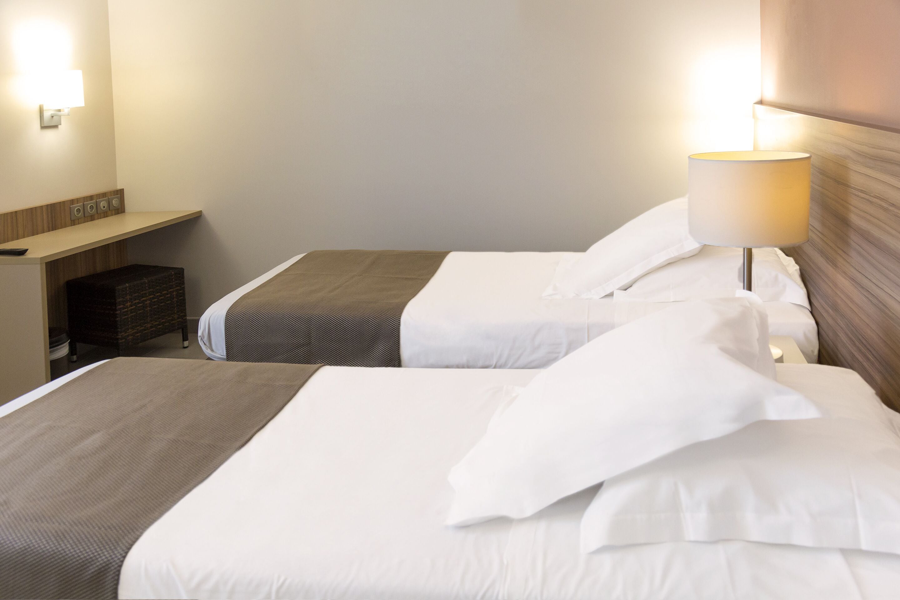Une chambre d’hôtel avec deux lits, une table de chevet, une lampe et un luminaire fixé au mur.
