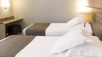 Une chambre d’hôtel avec deux lits, une table de chevet, une lampe et un luminaire fixé au mur.