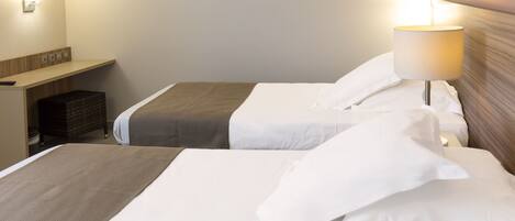 A hotel room with two beds, a bedside table, a lamp, and a wall-mounted light fixture.