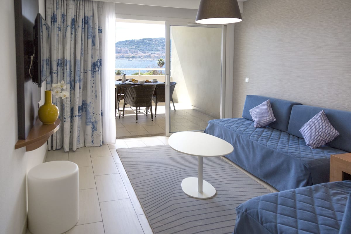 Ein modernes Zimmer mit einem blauen Sofa, einem kleinen weißen Tisch und Meerblick durch eine Glastür.