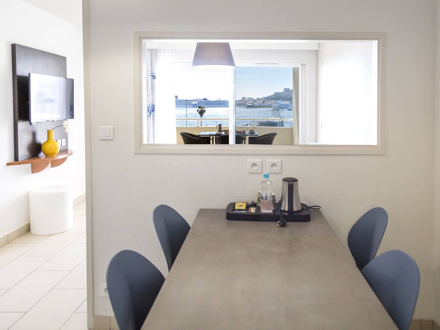 Un coin repas avec vue sur la mer, une table avec des chaises, une lampe et une petite étagère ornée d’un vase et d’une plante.