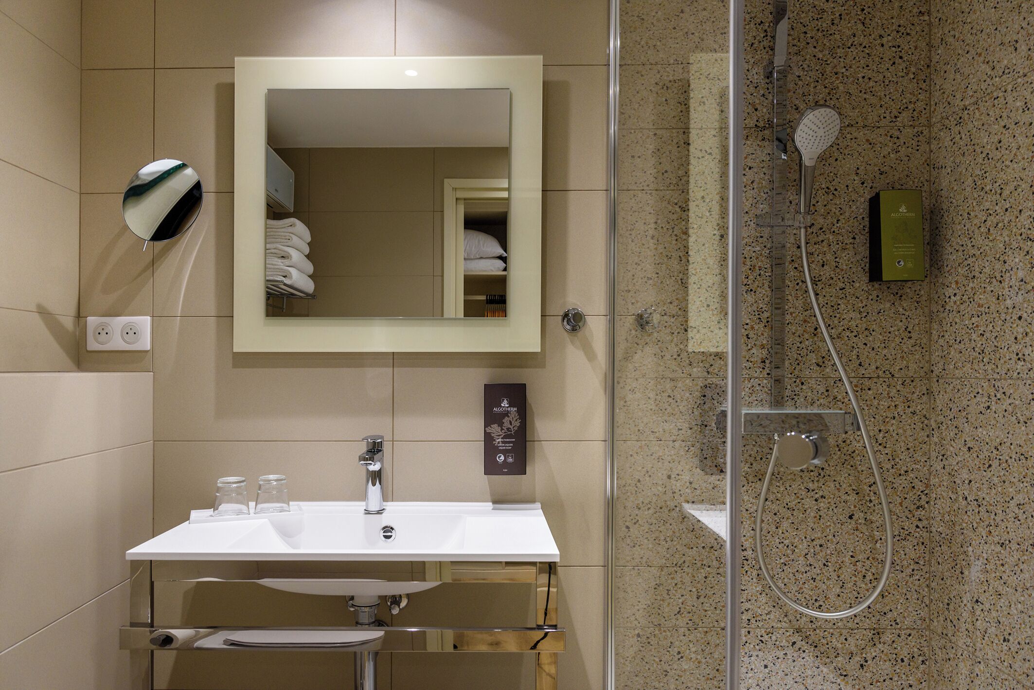 Un baño con un lavamanos blanco, un espejo, una ducha con cabezal de ducha manual y un perchero para toallas.