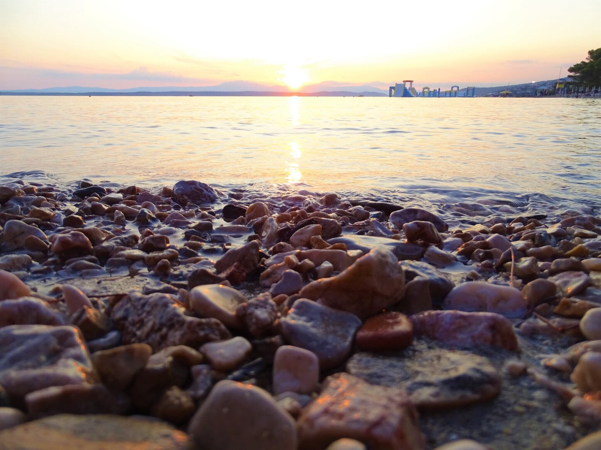 A beach with pebbles and a sunset in the background.