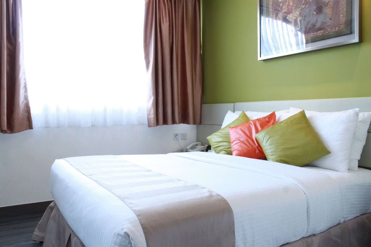 A neatly made bed with white linens and colorful pillows, a telephone on the nightstand, and a painting on the wall.