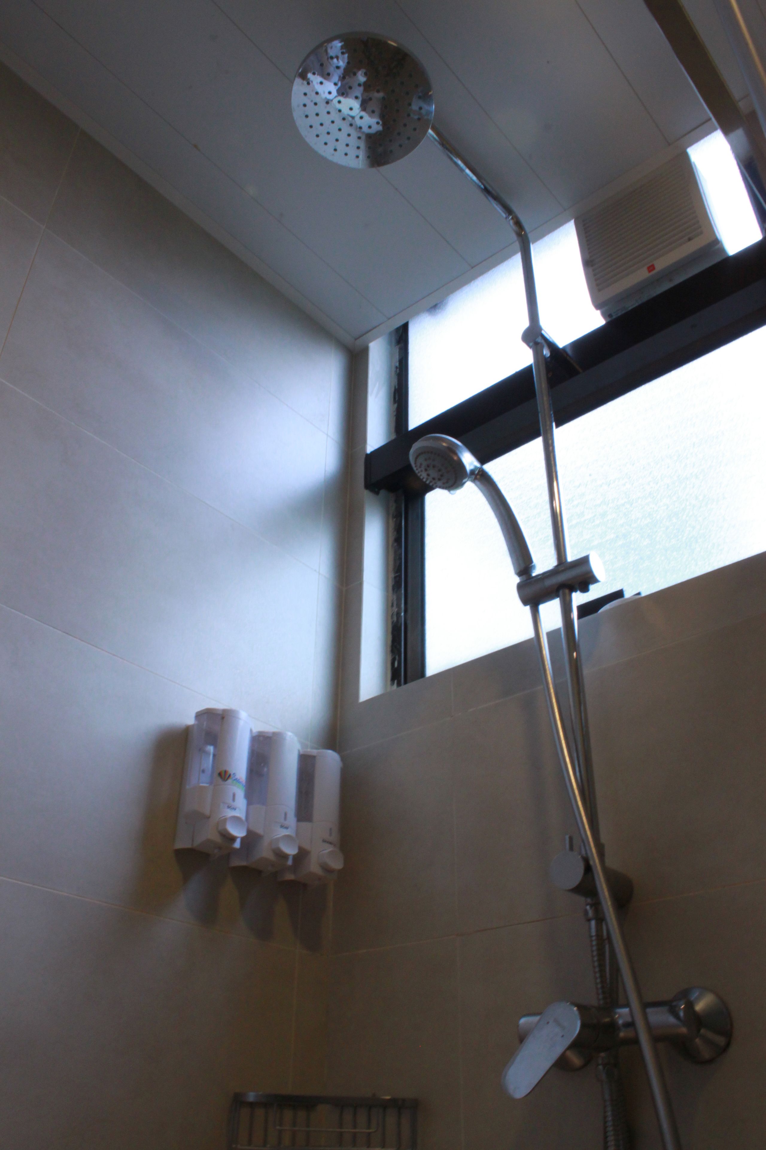 A shower with a handheld showerhead, a wall-mounted hand dryer, and a window above the shower.