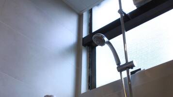 A shower with a handheld showerhead, a wall-mounted hand dryer, and a window above the shower.