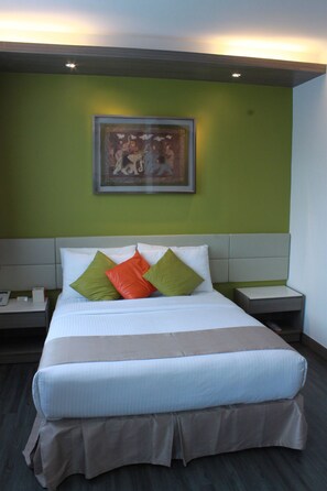 A neatly made bed with a white comforter and multiple pillows, a framed artwork above it, and a bedside table with a lamp. - Seaview Holiday Resort (Mui Wo)