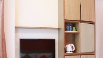 Habitación de hotel con cama, escritorio con computadora, televisor, taburete pequeño, mueble con botellas y tetera.