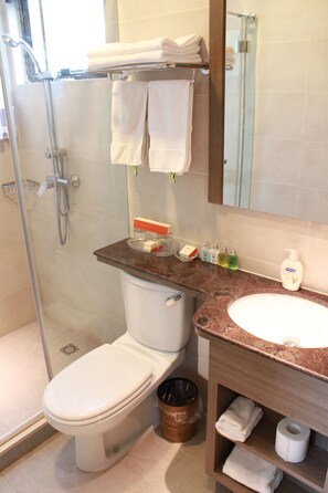 A bathroom with a toilet, sink, and shower. There are towels stacked on a shelf, soap dispensers, and a trash can. - Seaview Holiday Resort (Mui Wo)