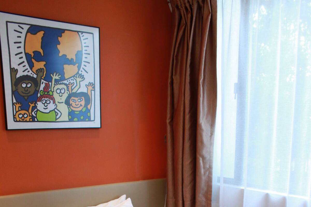 A neatly made bed with white and green pillows, a plain wall, and a window with curtains.