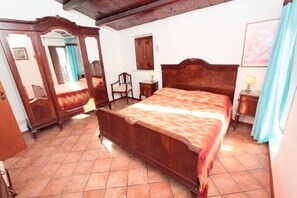 A bedroom with a wooden bed, a mirror, a chair, and a small table. - Casa Ifigenia (Cefalù)