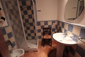 A bathroom with a checkered tile pattern, a shower, a sink, a chair, and a mirror. - Casa Ifigenia (Cefalù)