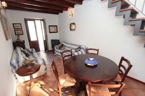 A dining area with a round wooden table, six chairs, and a striped sofa. - Casa Ifigenia (Cefalù)