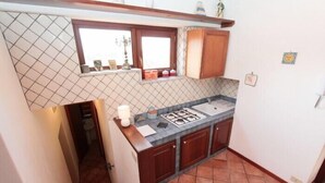 A compact kitchen with a gas stove, wooden cabinets, and a tiled backsplash. - Casa Ifigenia (Cefalù)