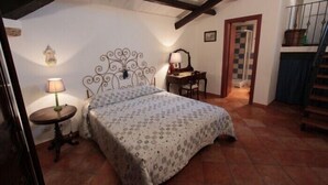 A bedroom with a bed, a nightstand, a lamp, a dresser, and a staircase. - Casa Ifigenia (Cefalù)