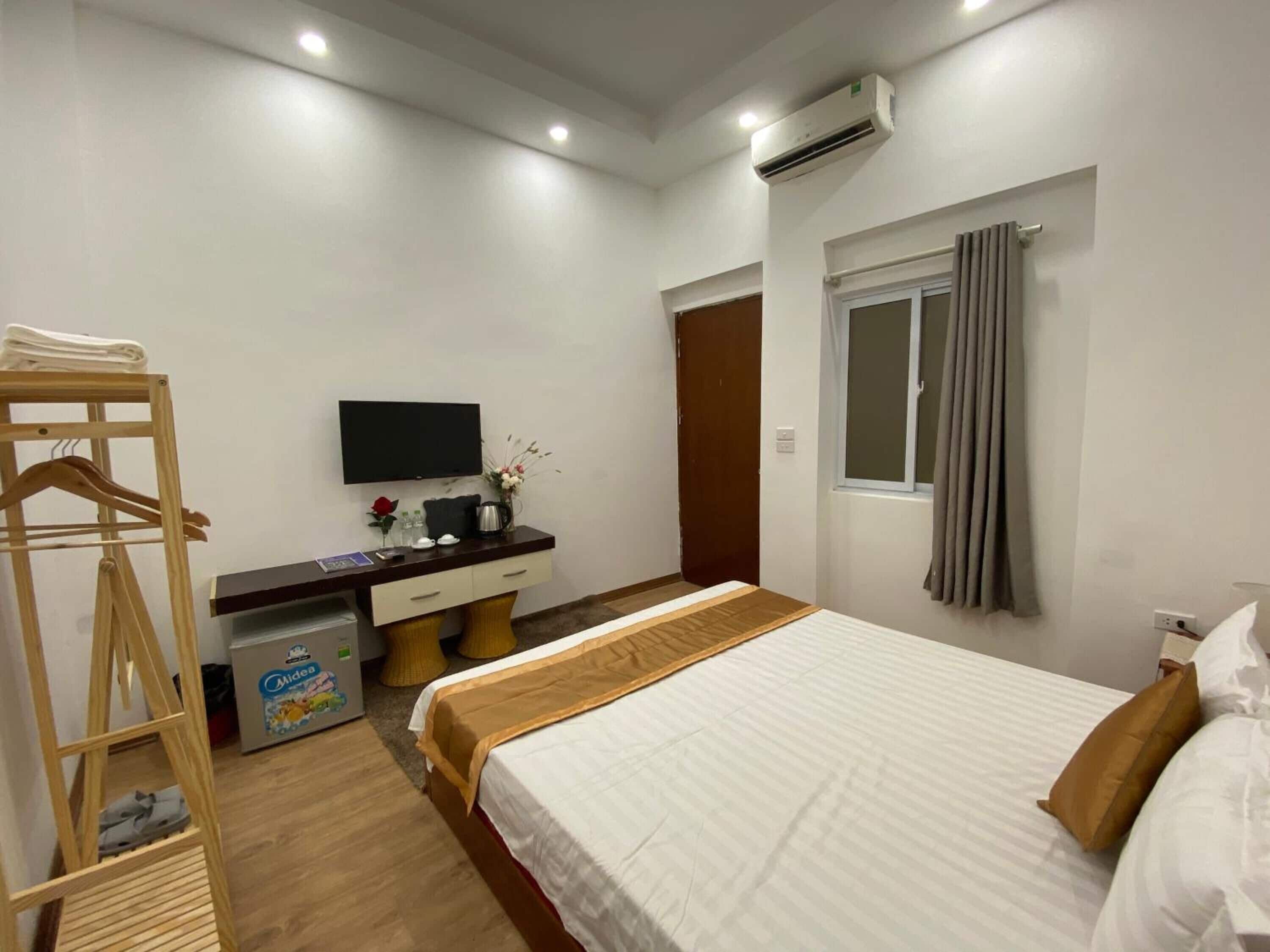 Habitación de hotel con cama, escritorio con televisor de pantalla plana, armario, ventana con cortinas y equipo de aire acondicionado.