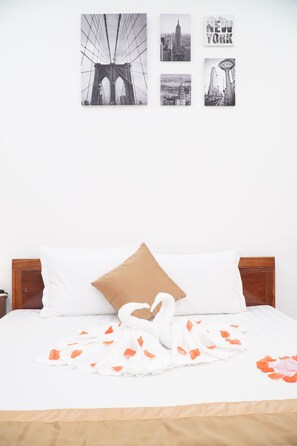 A hotel room with a bed, white pillows, a brown pillow, a white towel, and orange flower petals on the bed. There are four black and white pictures on the wall. - Thuc at 3am (Hanoi)