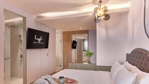 Una habitación de hotel moderna con una cama grande, televisión, ducha y espejo.