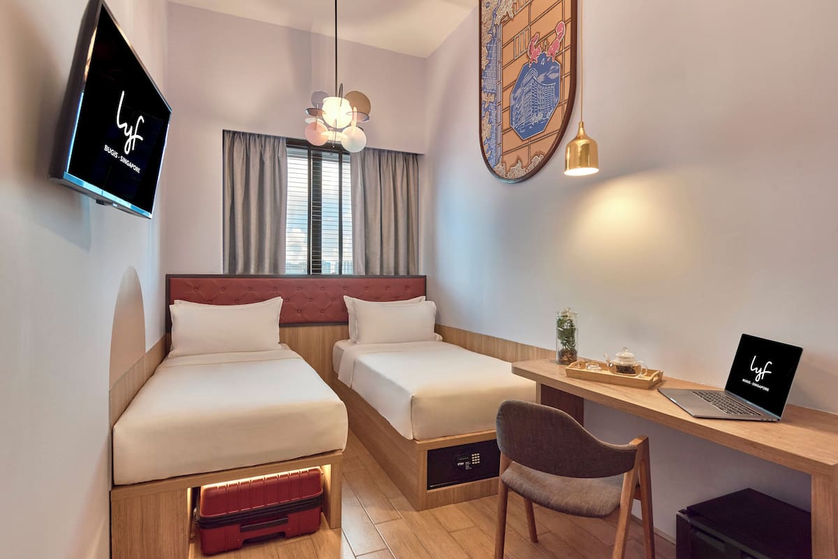 Une chambre d’hôtel avec deux lits, un bureau avec un ordinateur portable, une télévision et un élément décoratif mural.