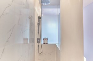 A modern bathroom with a glass-enclosed shower, marble tiles, and a window with bottles of shampoo and conditioner. - lyf Bugis Singapore (Singapore)