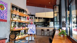 Interior de un restaurante con barra, mesas y una cocina visible a través de una puerta abierta.
