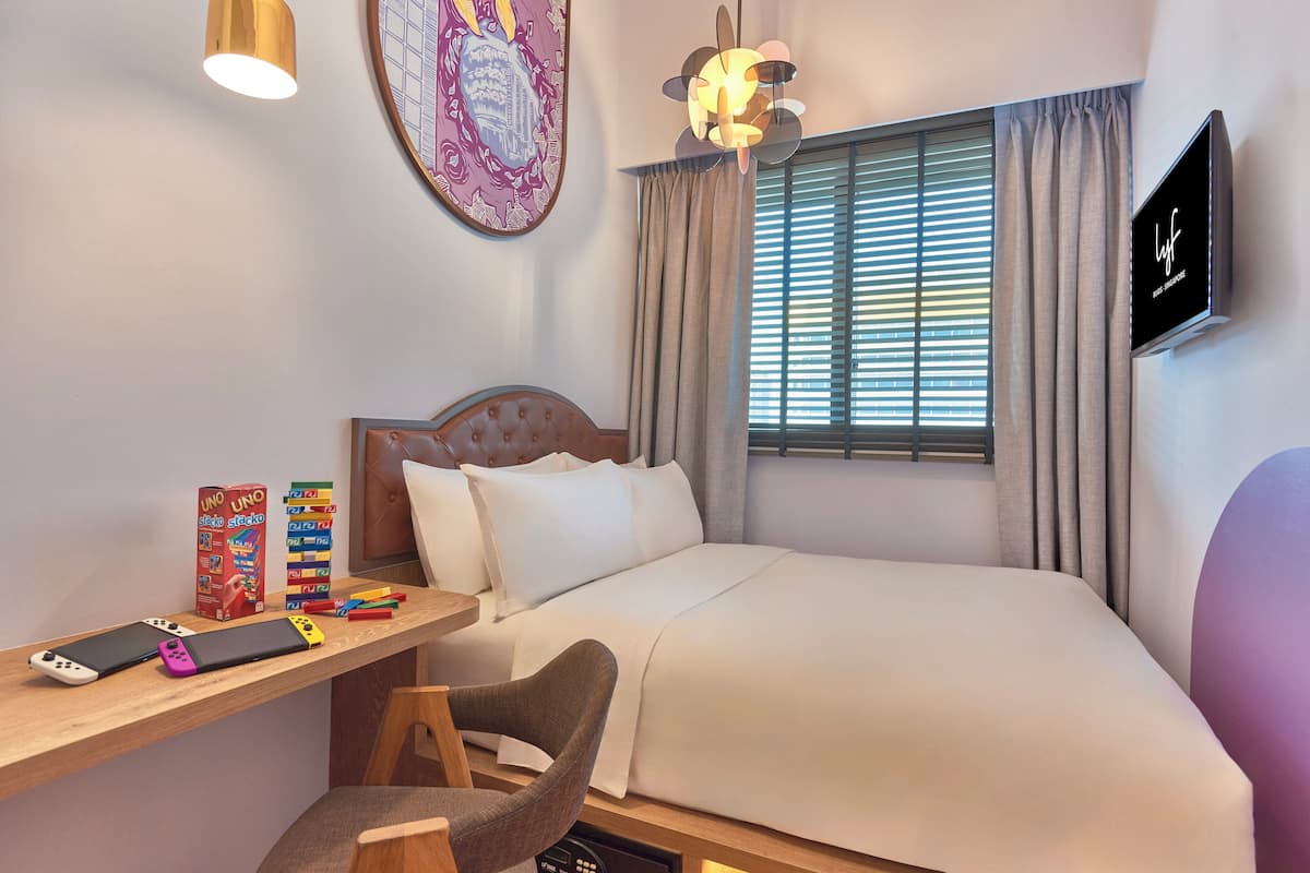 Une chambre d’hôtel bien rangée, avec un lit, un bureau et une chaise, une télévision et une fenêtre avec des rideaux.