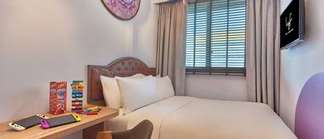 Habitación de hotel ordenada con una cama, un escritorio con silla, un televisor y una ventana con cortinas.