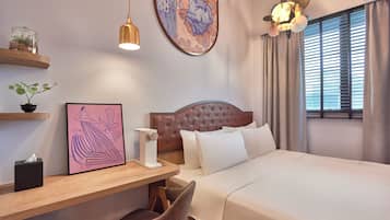 Ein Hotelzimmer mit Bett, Schreibtisch mit Stuhl, Nachttisch, Blumentopf, gerahmtes Bild und einem großen Fenster mit Vorhängen.