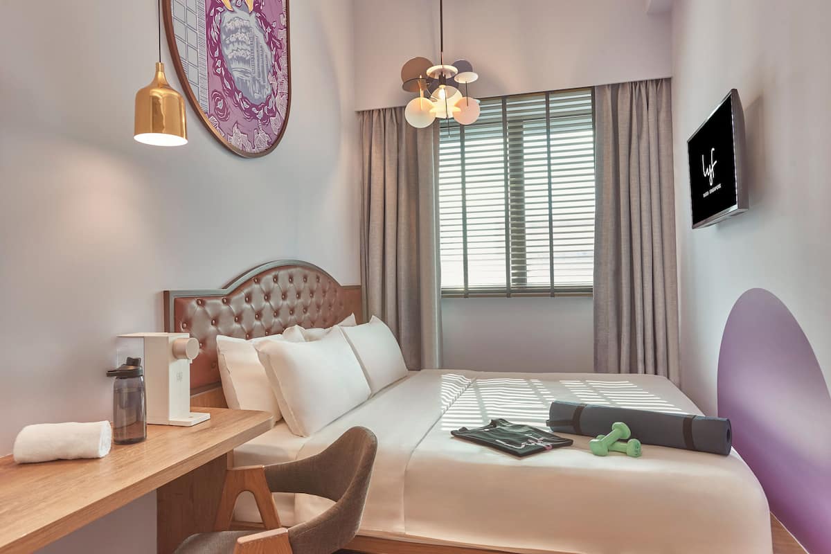 Une chambre d’hôtel moderne équipée d’un lit, d’un bureau, d’une chaise, d’une machine à café, d’une bouteille d’eau, d’un tapis de yoga et d’haltères.