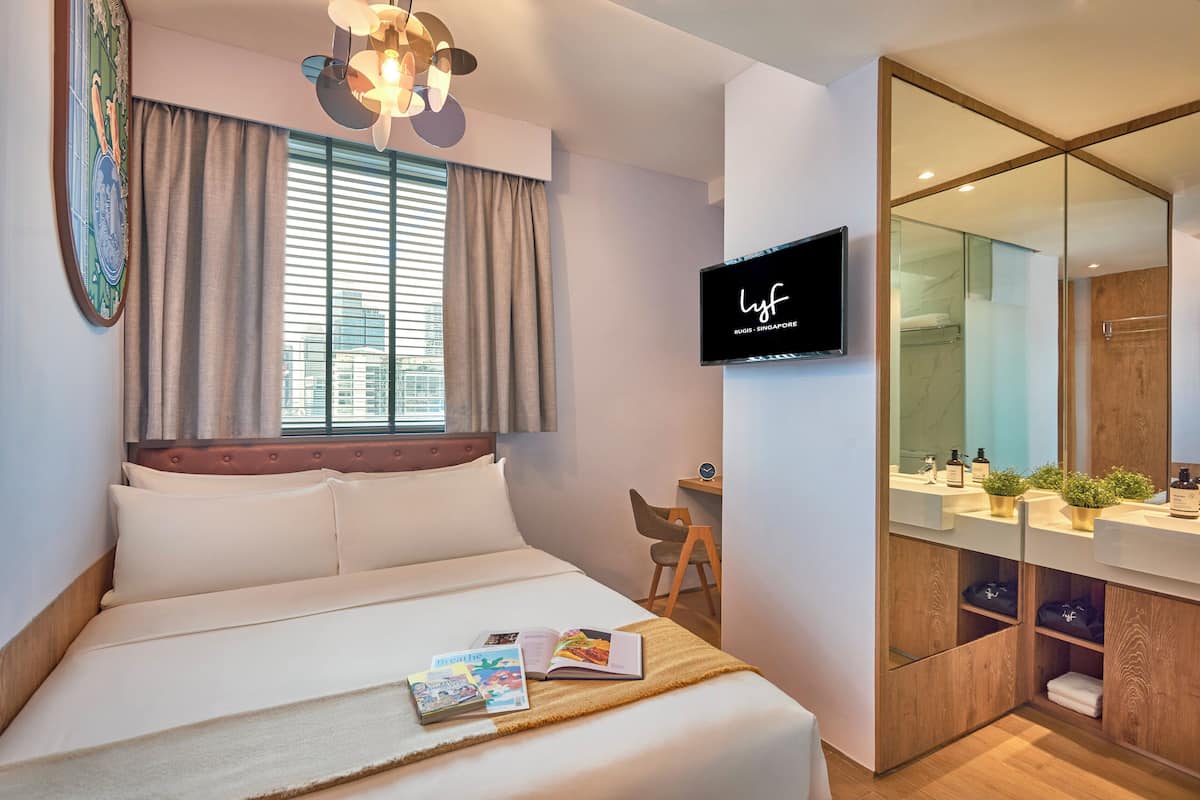 Une chambre d’hôtel moderne équipée d’un lit, d’un bureau, d’une télévision et d’une salle de bain avec un miroir et un lavabo.