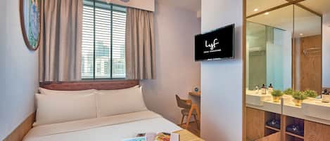 A modern hotel room with a bed, a desk, a TV, and a bathroom with a mirror and sink.