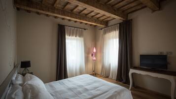 Une chambre avec un plafond en bois, un lit recouvert de draps blancs, une table de chevet avec une lampe et un téléviseur posé sur un meuble.