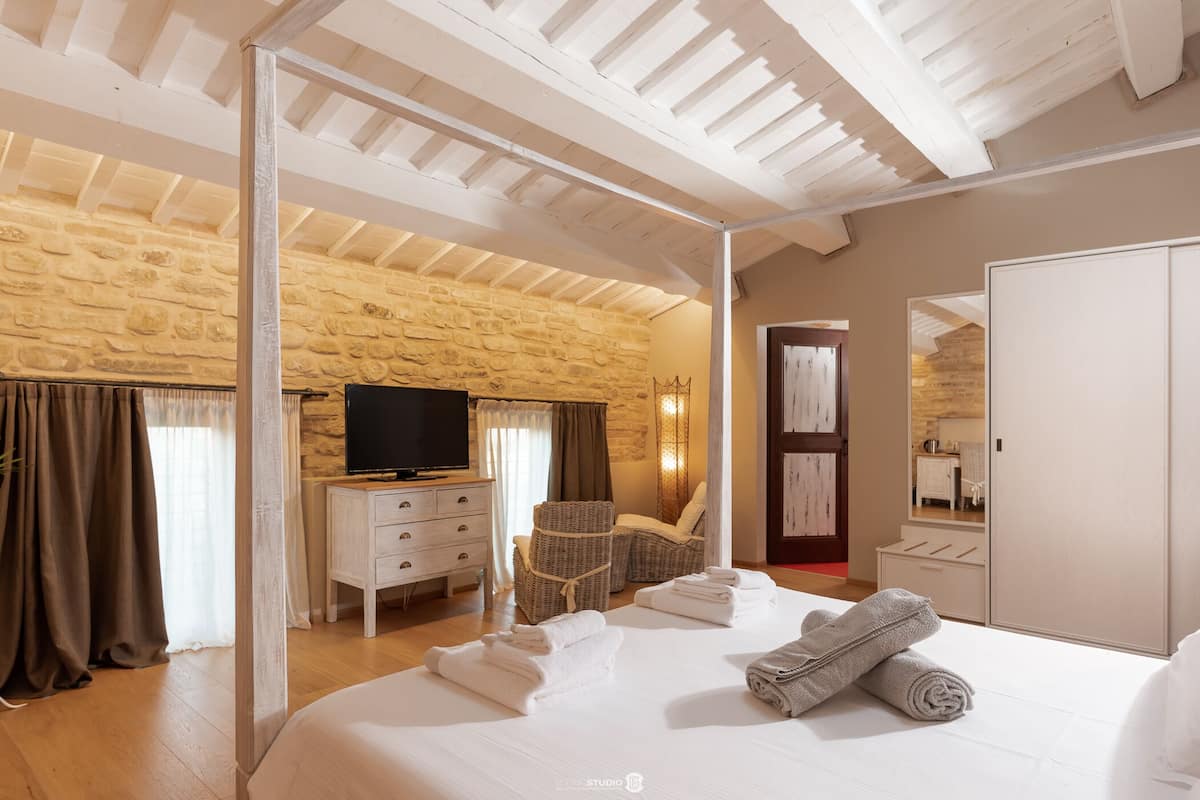 Habitación de hotel con pared de piedra, una cama, televisor, una silla y un armario.