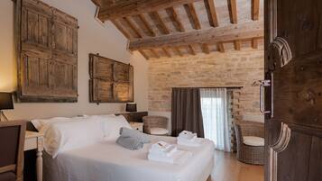 Un dormitorio con una cama grande, vigas de madera, paredes de piedra, sillas de mimbre y una puerta.