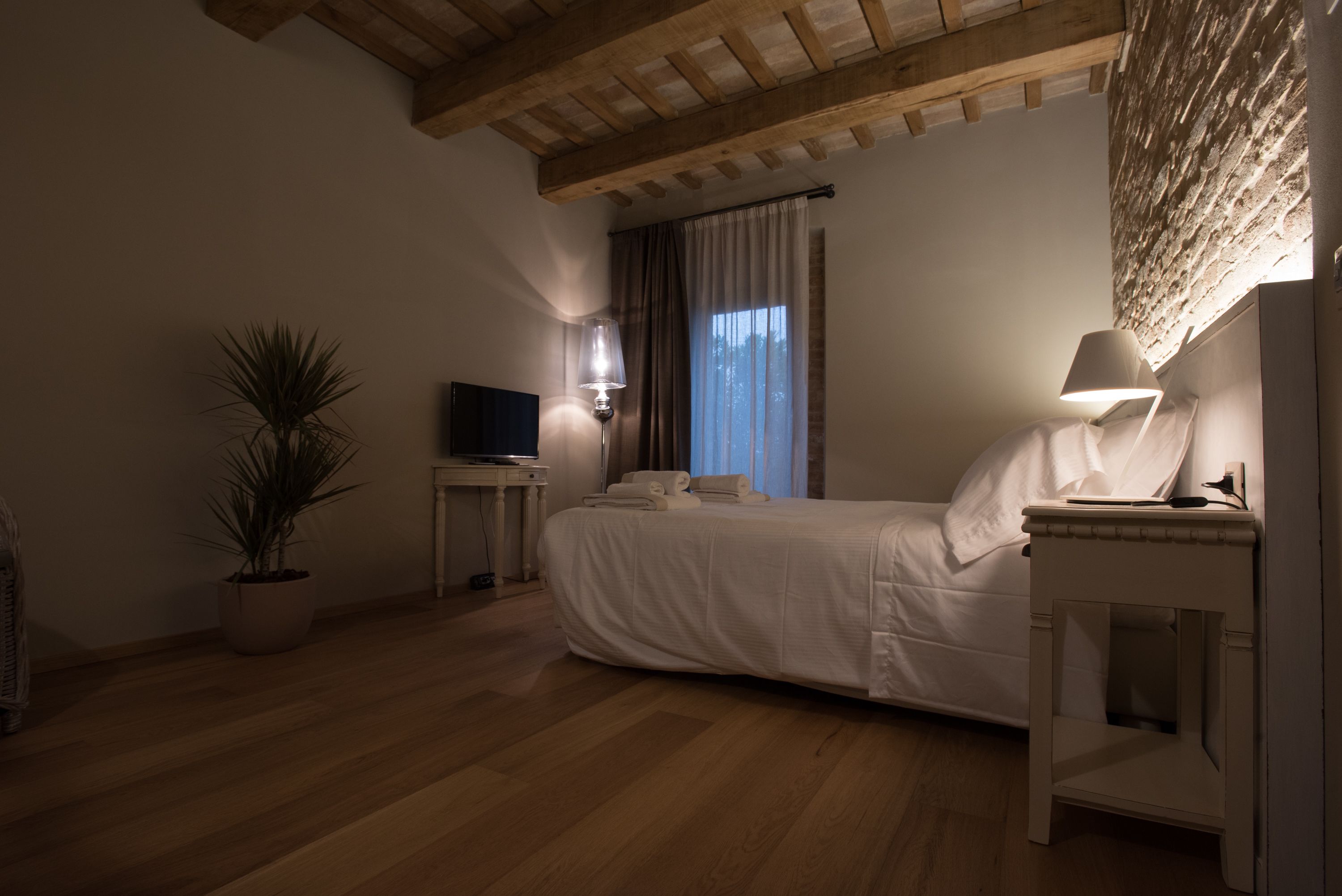 Ein Schlafzimmer mit einem Bett, einem Fernseher, einer Lampe, einem Topf mit Pflanze und einer Holzbalkendecke.