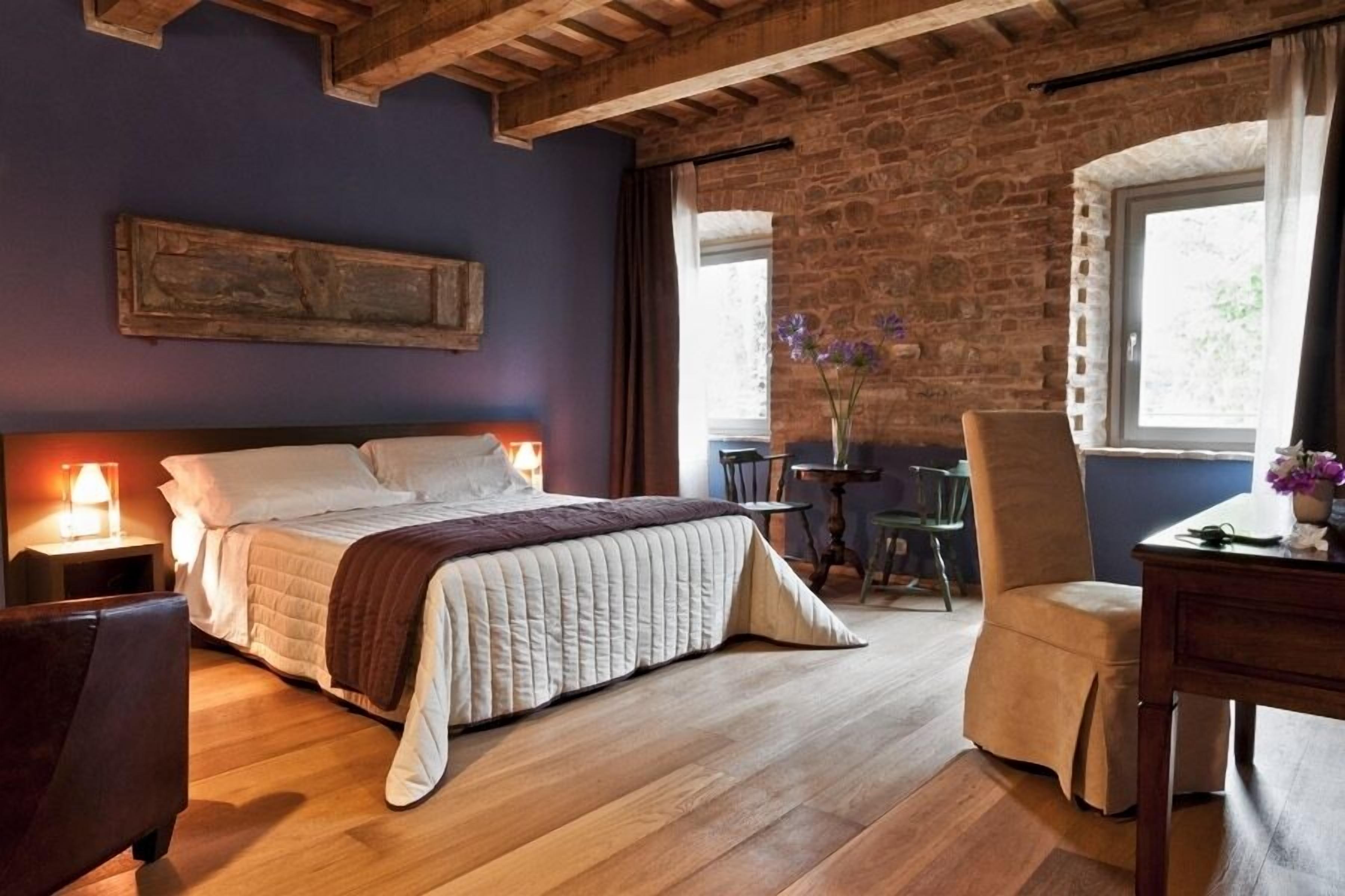 A cozy bedroom with a wooden bed, a nightstand, a chair, and a desk with a vase of flowers.