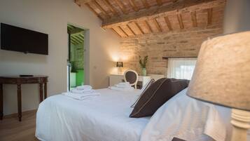 A bedroom with a large bed, a flat-screen TV mounted on the wall, a wooden table, and a brick wall.