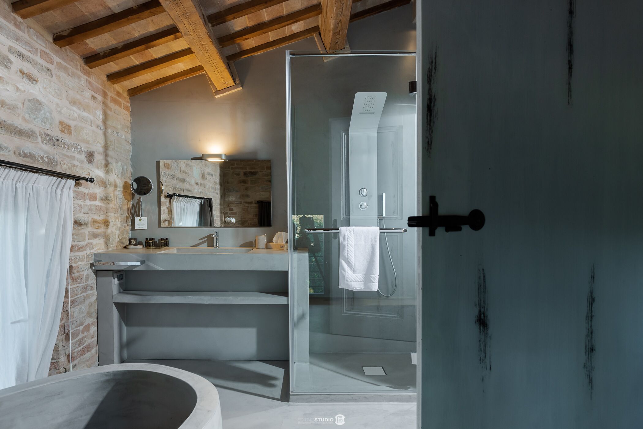 A modern bathroom with a stone wall, a glass shower enclosure, and a large bathtub.