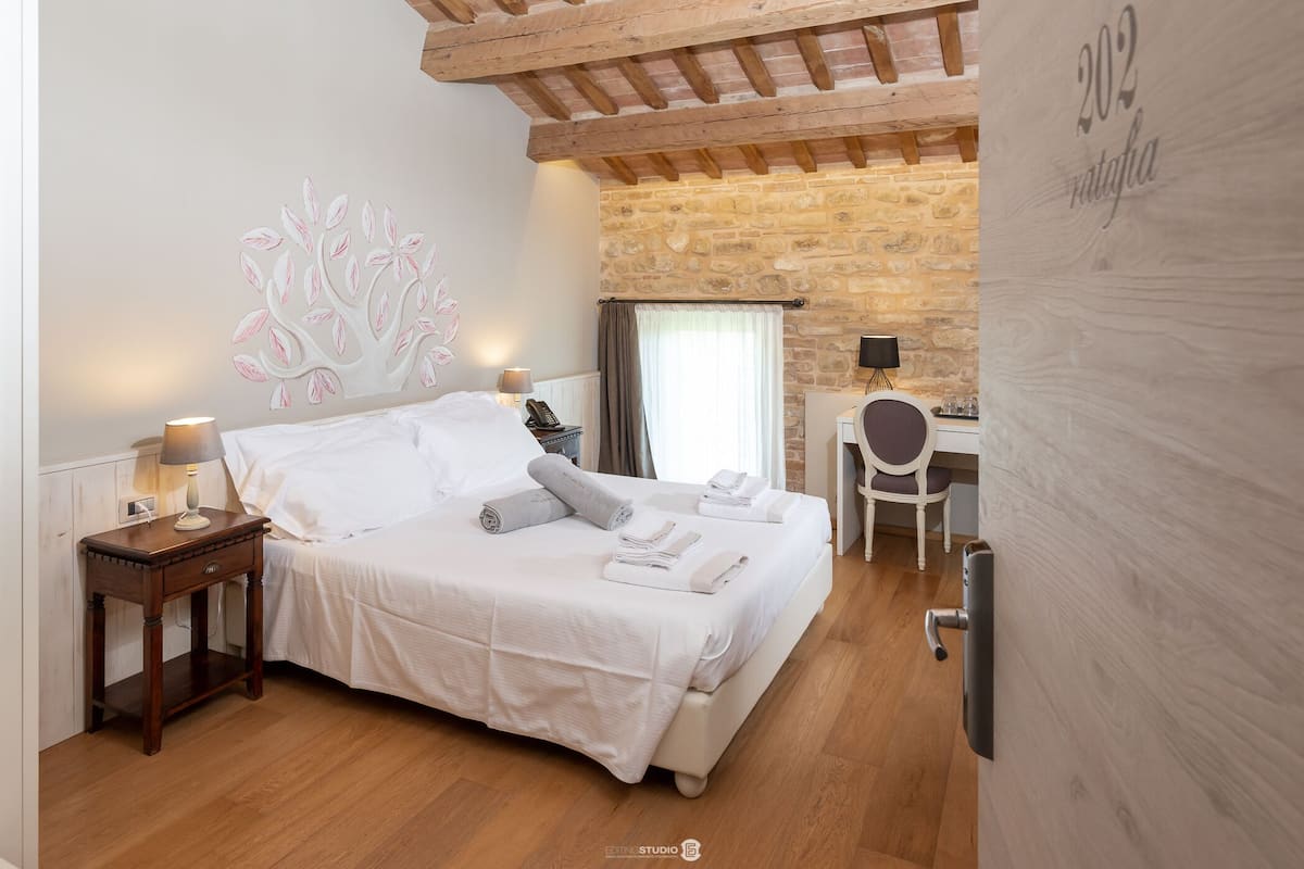 Un dormitorio con cama, mesita de noche, lámpara y pared de piedra.