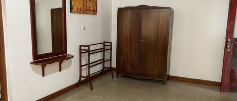 A room with a large wooden wardrobe, a mirror, and a small shelf.