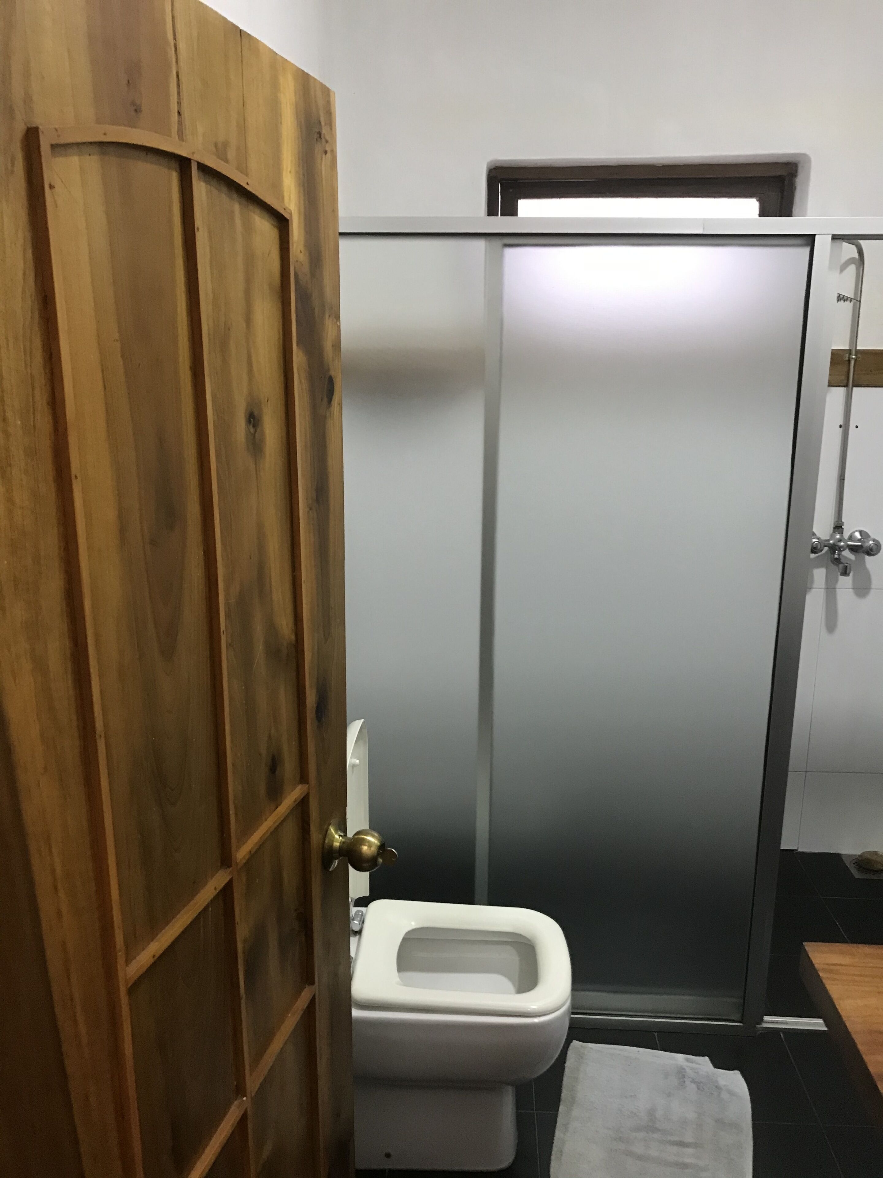 A bathroom with a wooden door, a white toilet, and a towel on the floor.