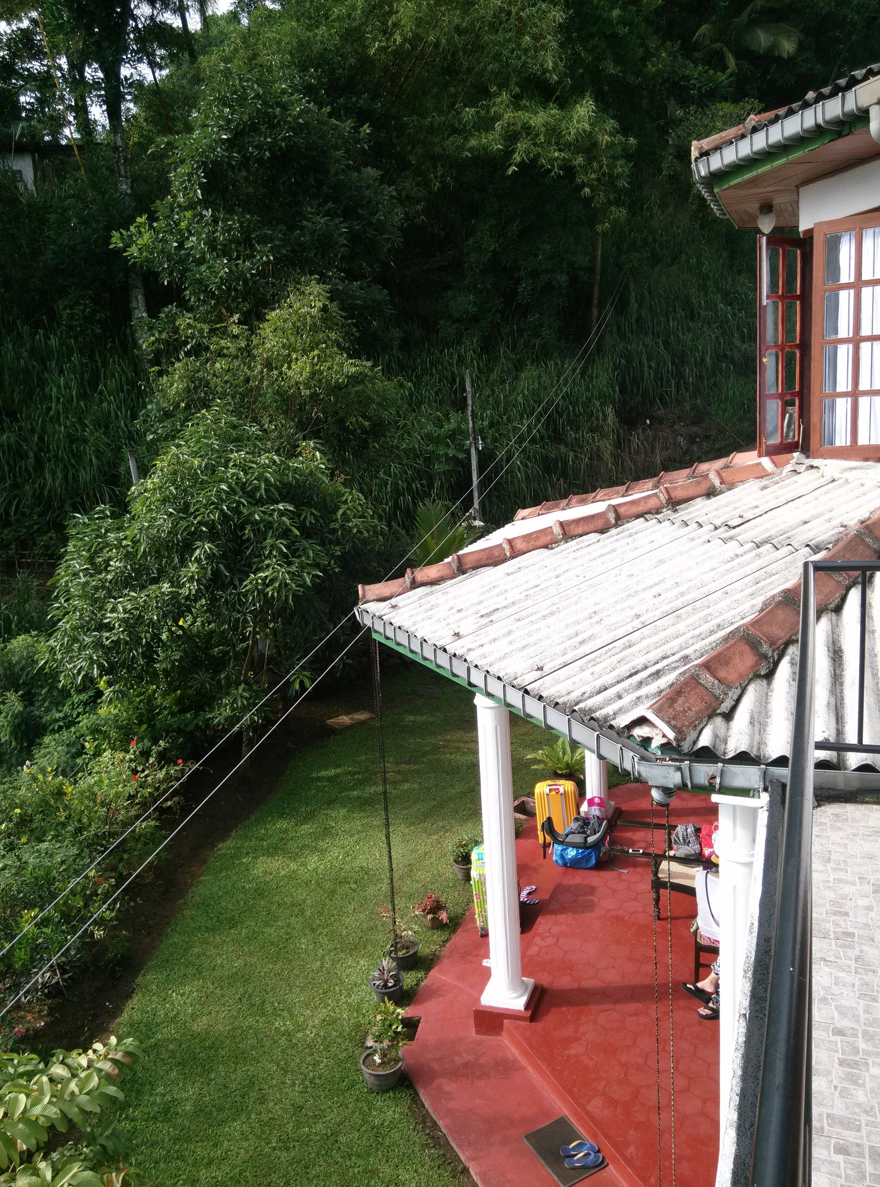 Ein Haus mit rotem Dach, einer Veranda und einem Garten mit verschiedenen Pflanzen.