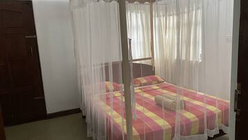 A room with a bed under a mosquito net, a wooden door, and a tiled floor.