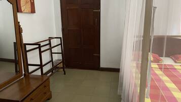 A bedroom with a wooden dresser, a door, and a bed with a checkered bedspread.