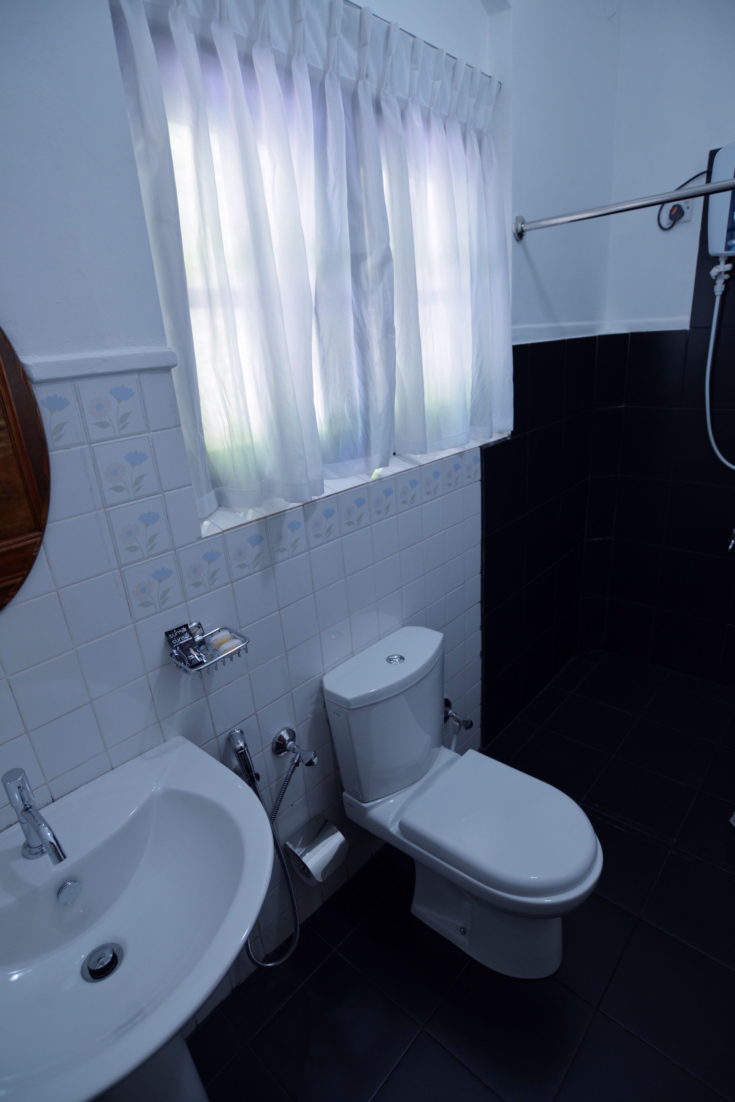 A bathroom with a toilet, sink, and a window with a curtain.