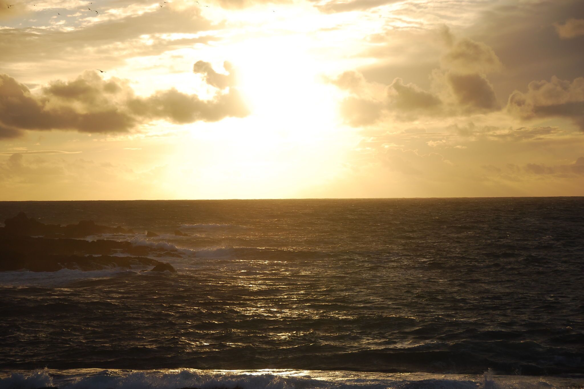 Ein Sonnenuntergang über dem Meer mit Wellen und Wolken.